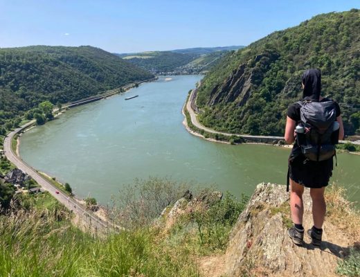 Eine Wandern steht beim alleine wandern auf einem Felsvorsprung hoch über dem Rhein.