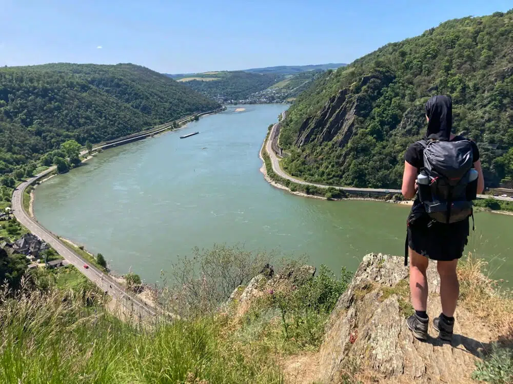 Eine Wandern steht beim alleine wandern auf einem Felsvorsprung hoch über dem Rhein.