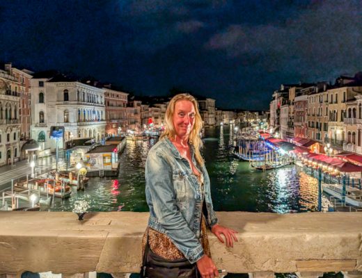 Sabine Schönberg steht abends auf der beleuchteten Rialtobrücke in Venedig, im Hintergrund der Canal Grande bei Nacht mit glitzernden Lichtern.