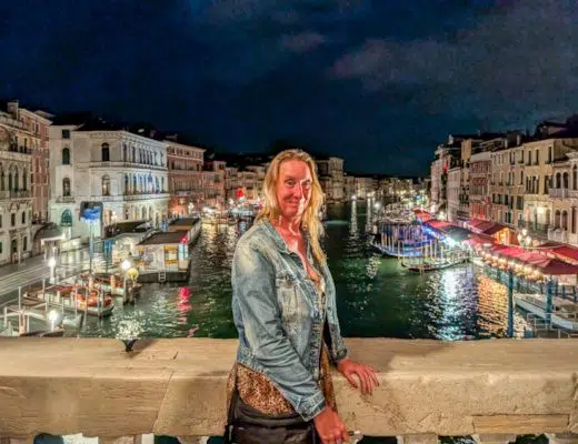 Sabine Schönberg steht abends auf der beleuchteten Rialtobrücke in Venedig, im Hintergrund der Canal Grande bei Nacht mit glitzernden Lichtern.
