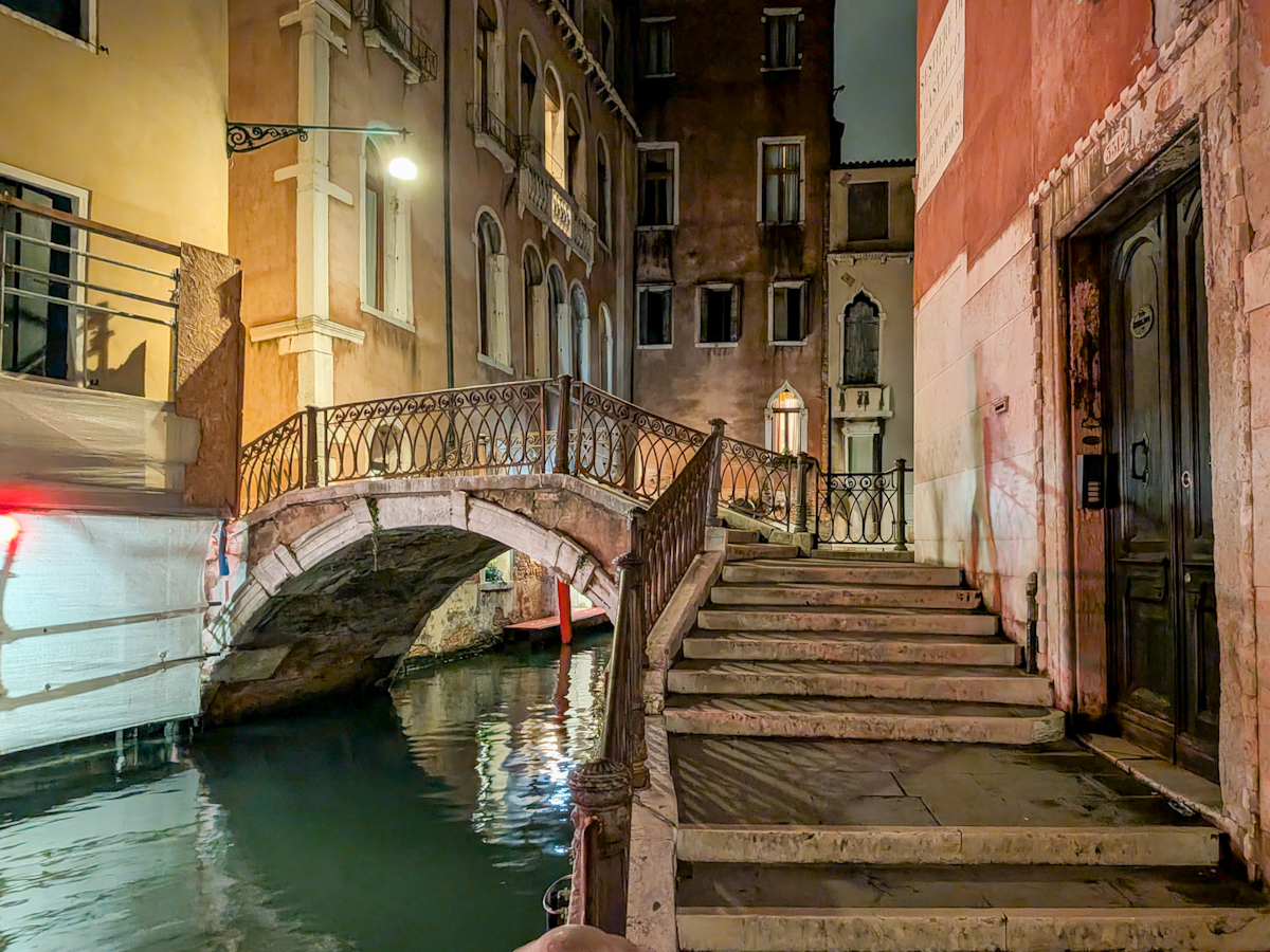 Kleine beleuchtete Brücke über einen ruhigen Kanal in Venedig bei Nacht