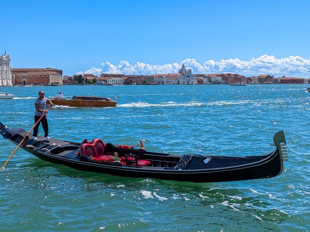 Gondel mit Gondoliere auf dem offenen Wasser der Lagune von Venedig, im Hintergrund die Skyline und ein Wassertaxi - Venedig-Tipps