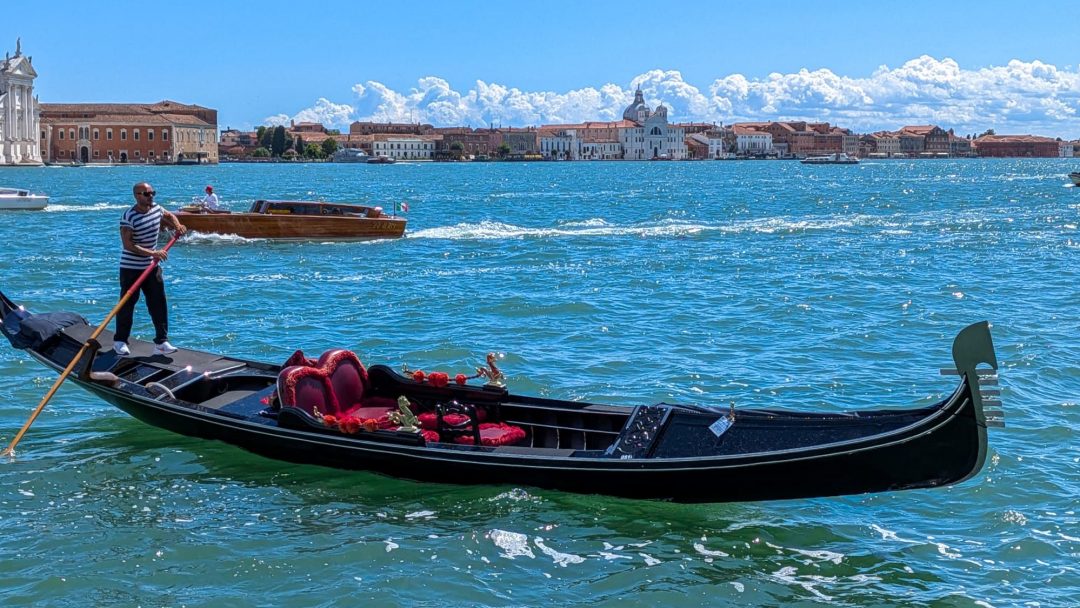 Gondel mit Gondoliere auf dem offenen Wasser der Lagune von Venedig, im Hintergrund die Skyline und ein Wassertaxi - Venedig-Tipps