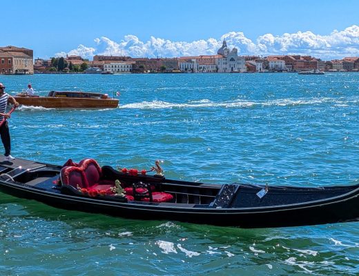 Gondel mit Gondoliere auf dem offenen Wasser der Lagune von Venedig, im Hintergrund die Skyline und ein Wassertaxi - Venedig-Tipps