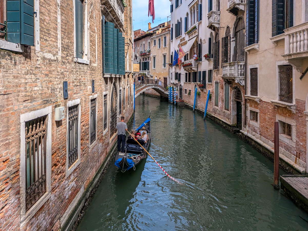 Schmaler Kanal in Venedig mit Gondel und bunten Palazzi im Sonnenlicht
