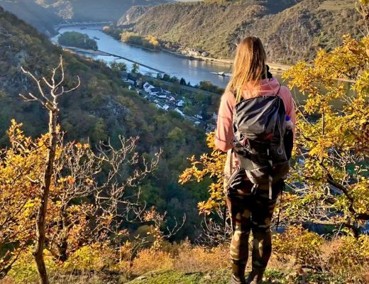 Wanderin mit Rucksack blickt im Herbst von einem Aussichtspunkt auf die Rheinschleife bei St. Goar - Symbolbild für die Verbindung von Wandern und Coaching.